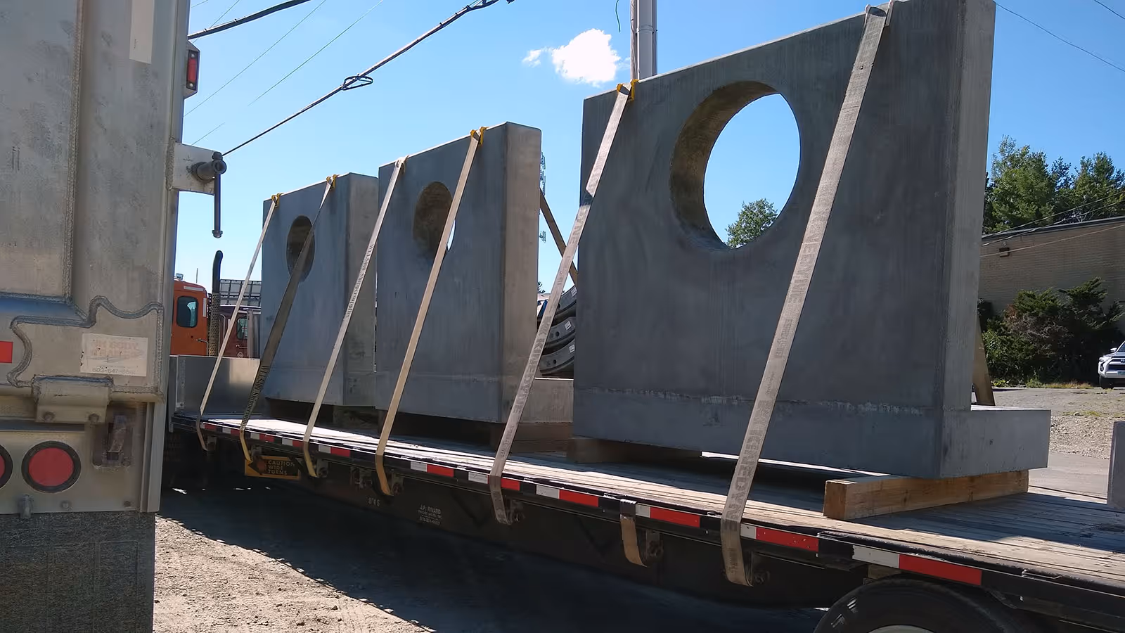 Three large concrete slabs with circular openings strapped on a flatbed truck trailer outdoors.
