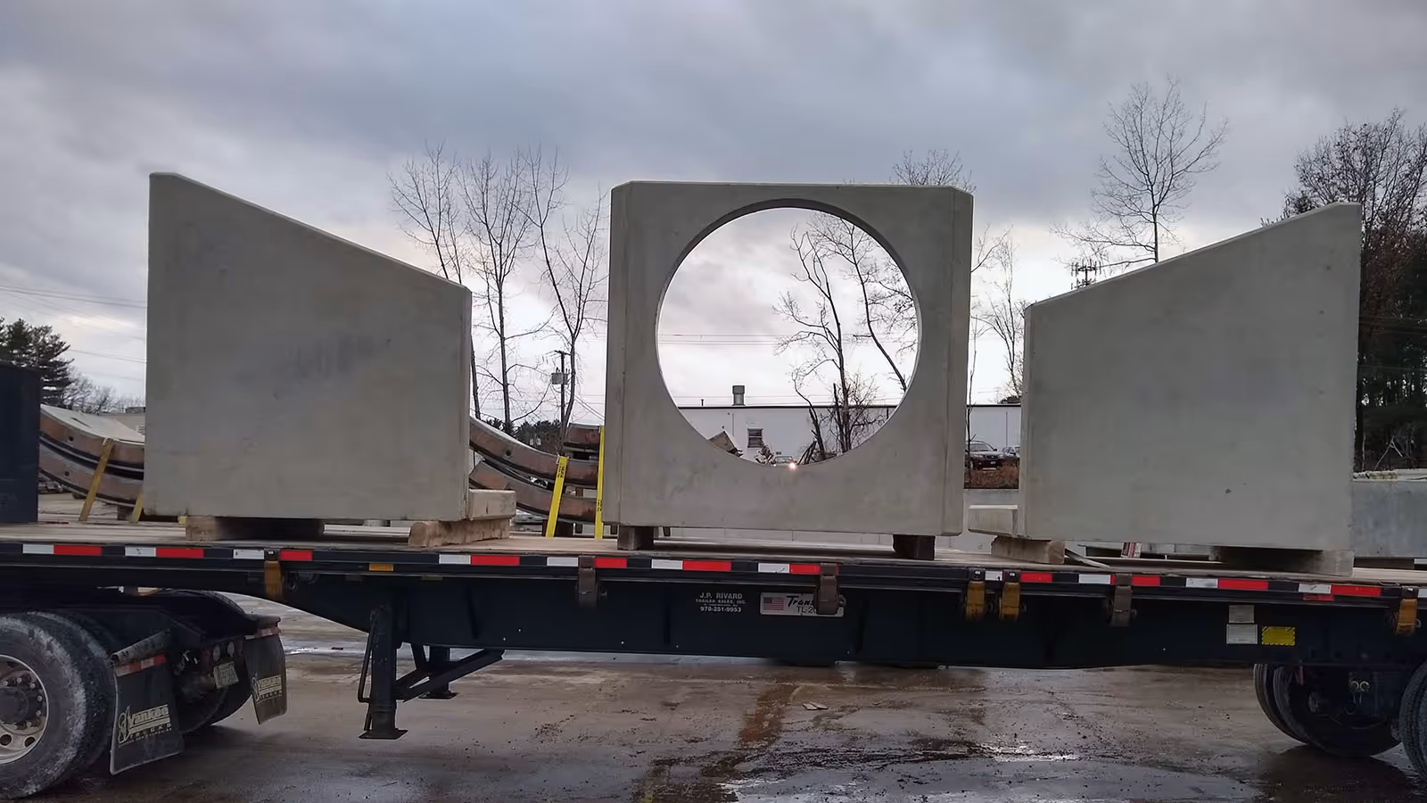 Three large precast concrete headwall sections loaded on a flatbed truck under a cloudy sky.