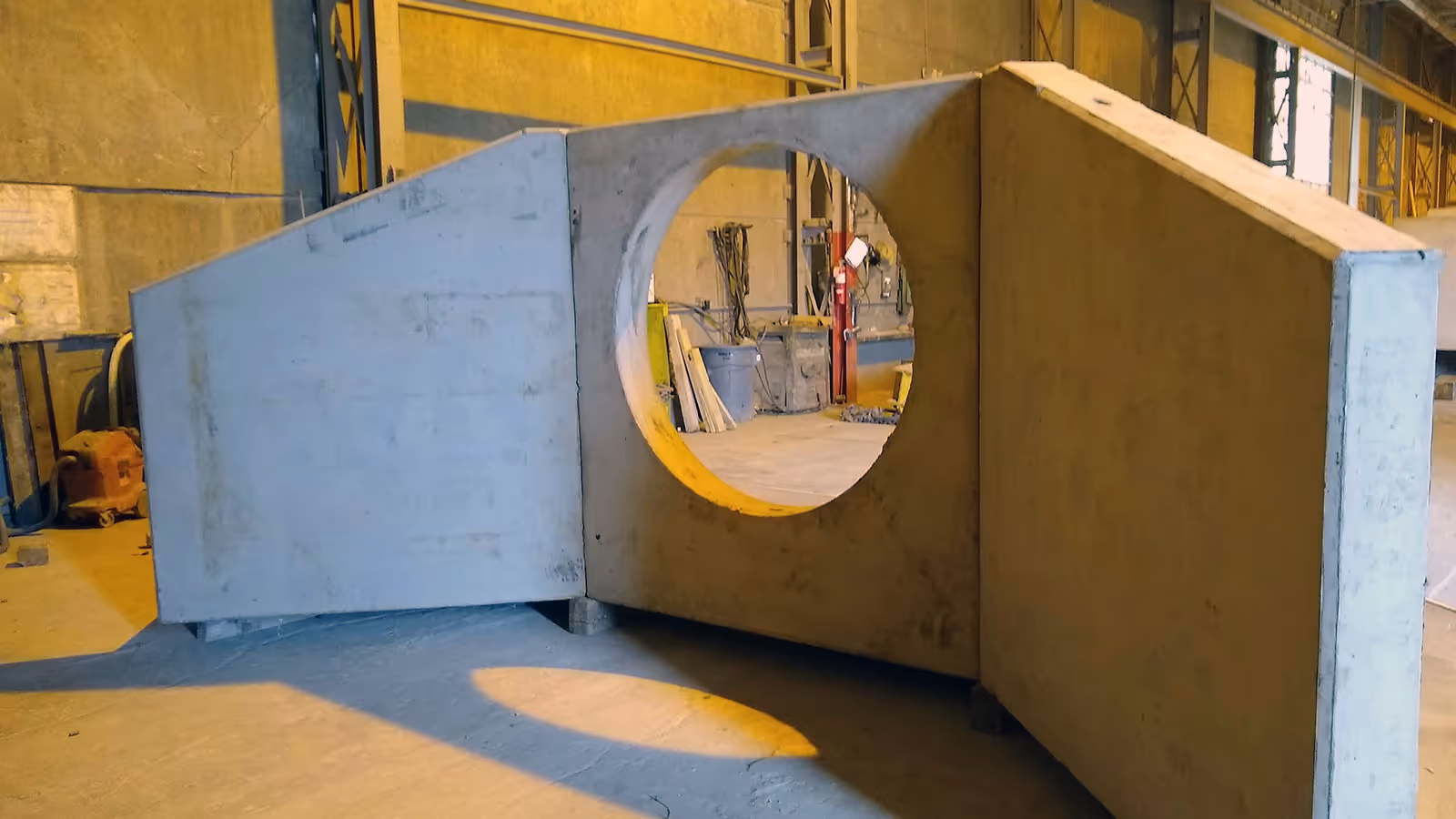 Large concrete structure with a circular opening in the center, inside an industrial warehouse.
