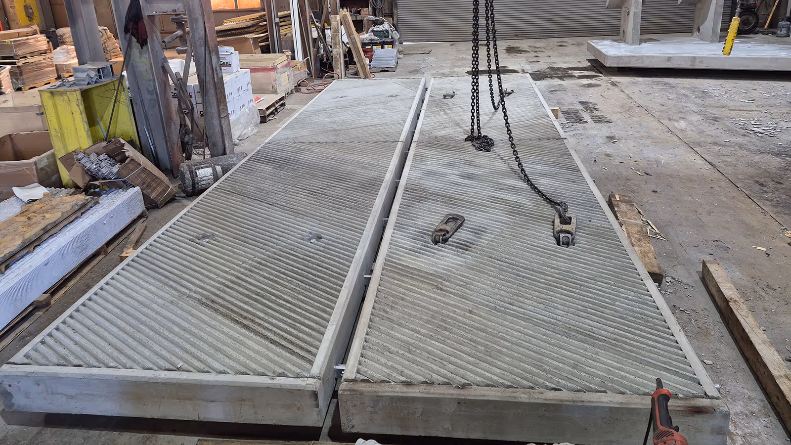 Two large ribbed concrete slabs lying on a warehouse floor with lifting chains attached to one slab.