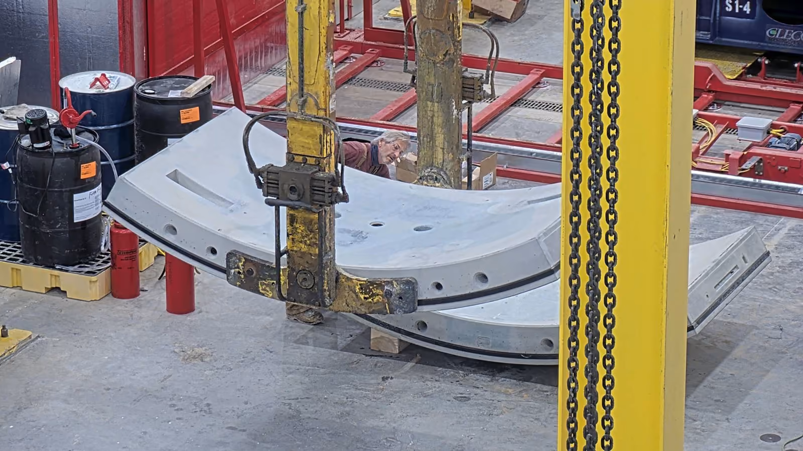 Two workers in blue helmets operate large red and yellow heavy machinery inside an industrial facility.
