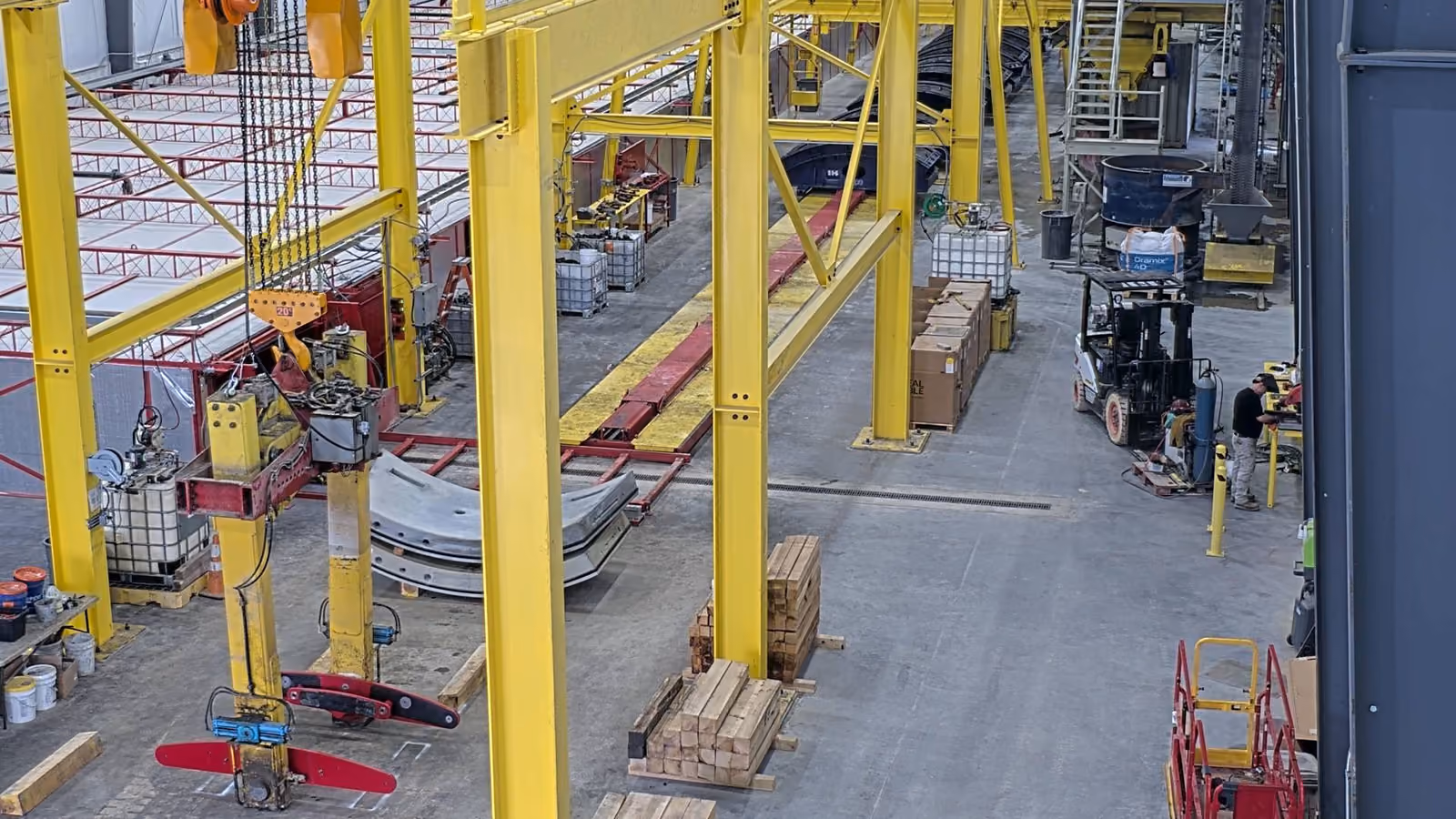 Industrial factory with yellow overhead cranes, stacked materials, and workers near machinery.