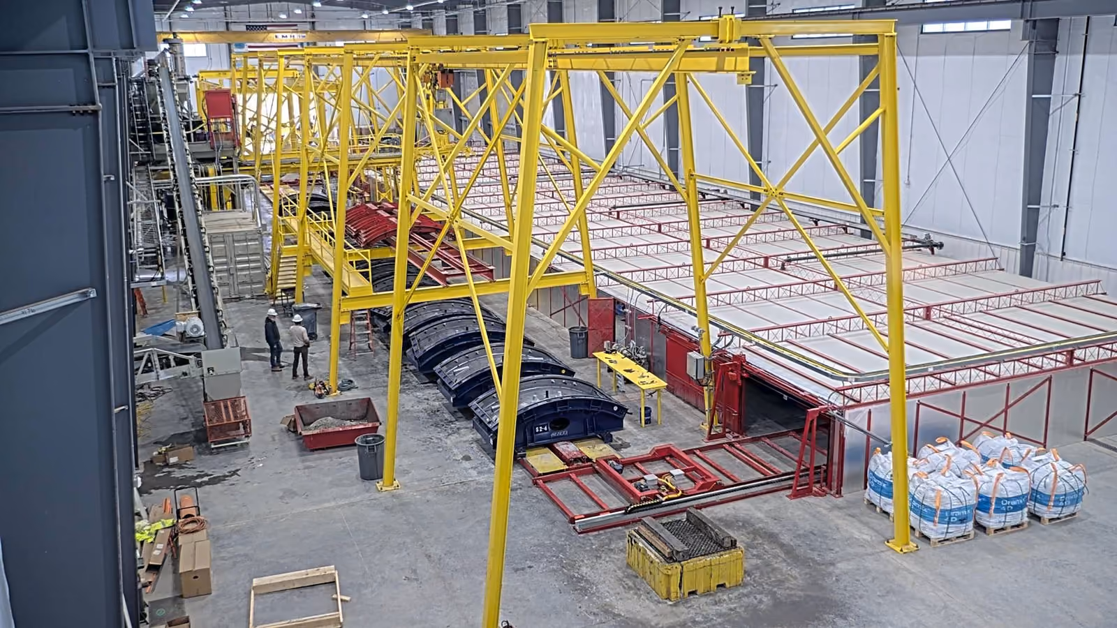 Industrial warehouse with yellow crane beams, forklift, stacked wood, and machinery on concrete floor.