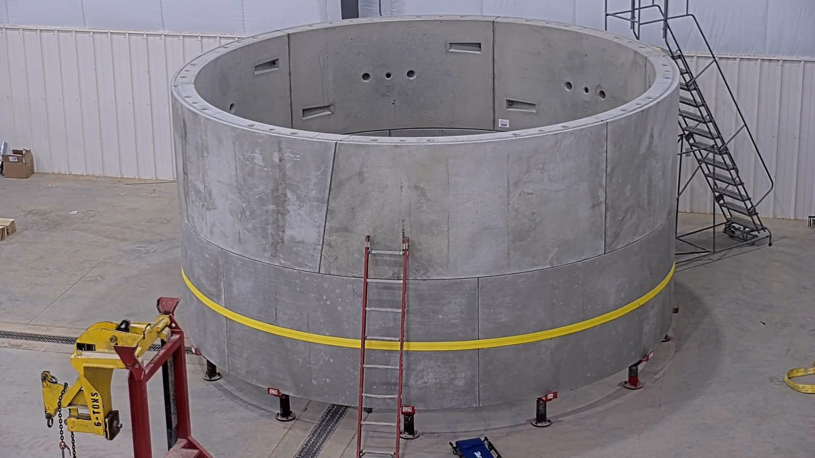 Industrial warehouse with yellow crane system, curved metal molds, and two workers in safety helmets.