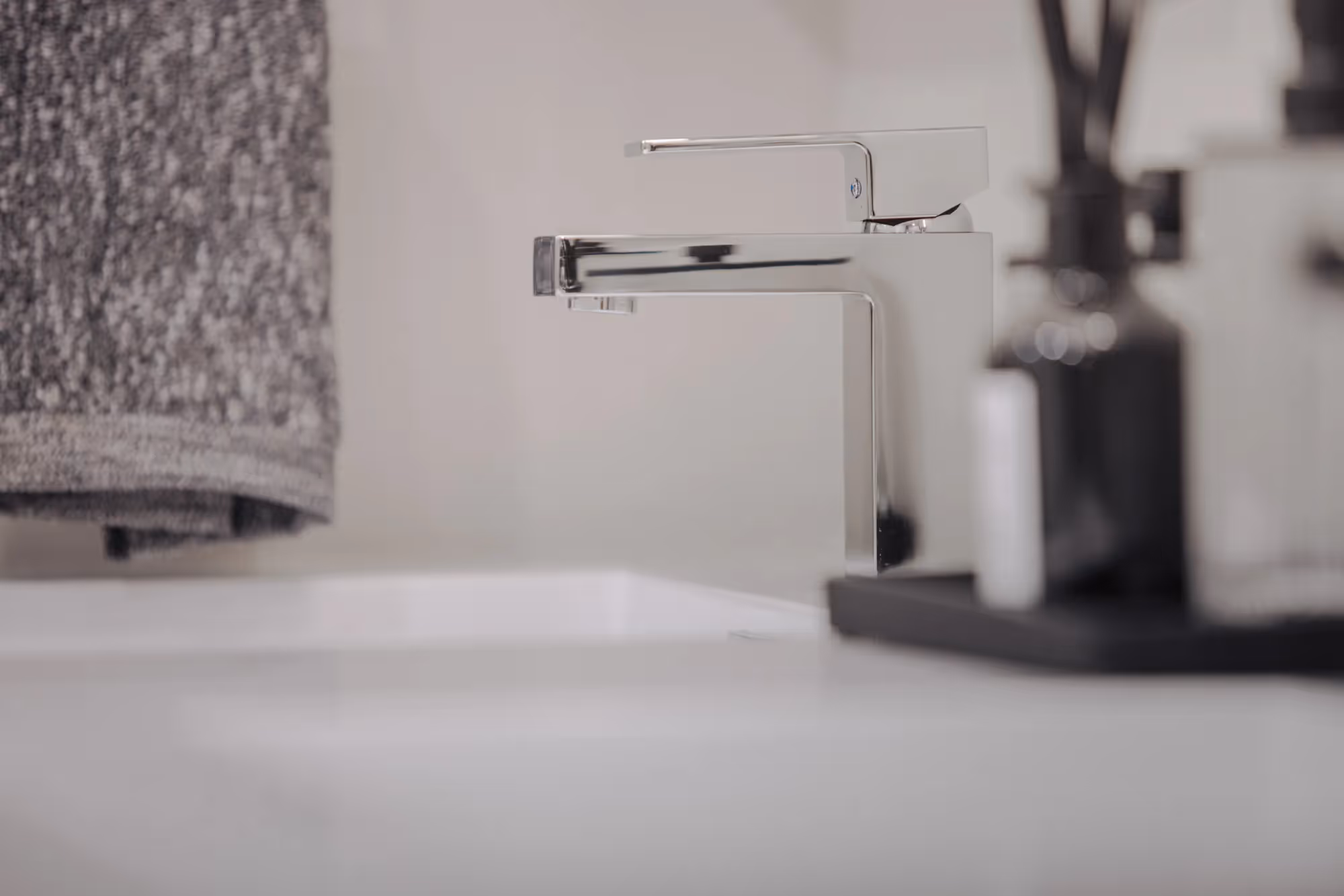 Close-up of a modern chrome bathroom faucet and sink, with a gray towel in the background, at The Julian apartments.