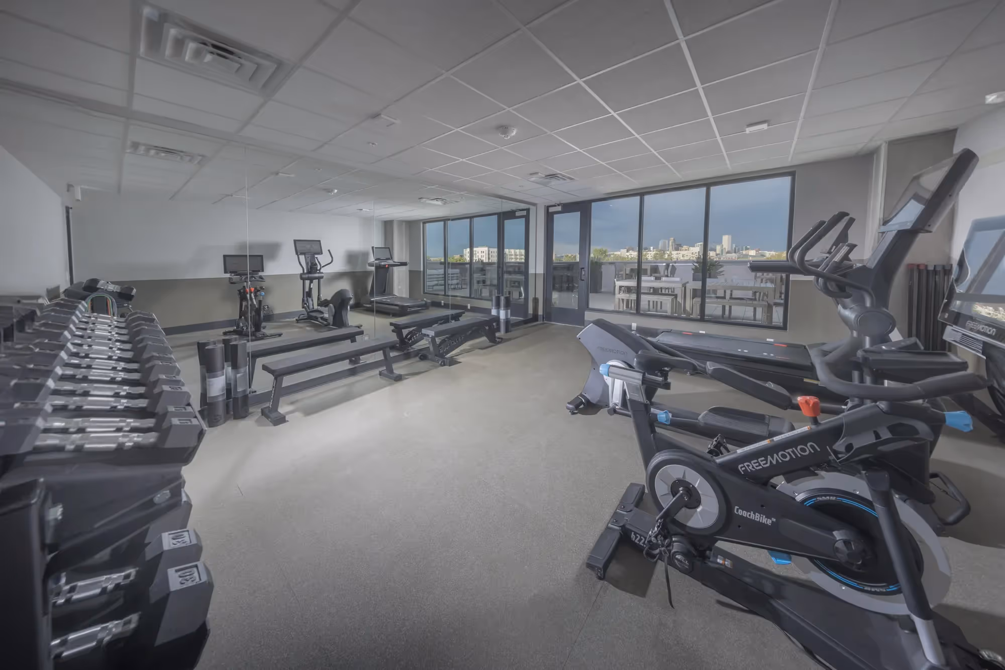 State-of-the-art fitness center at The Julian apartments in Sloans Lake, Denver, with cardio machines, free weights, and a view of the city skyline.