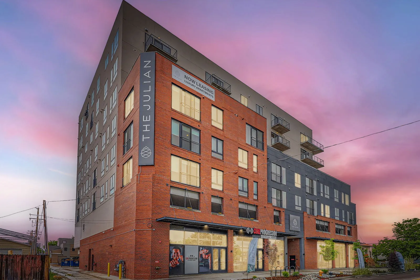 Modern brick and gray facade of The Julian luxury apartments in Sloans Lake, Denver, Colorado, at sunset, with a 'Now Leasing' banner visible.