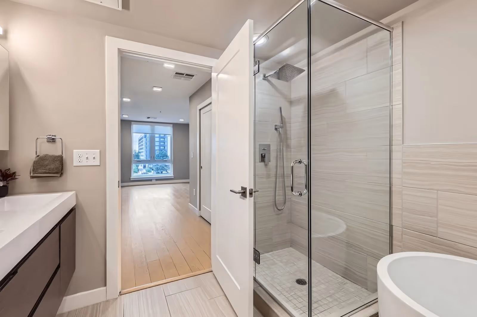 Modern bathroom with a glass walk-in shower and separate bathtub in a luxury apartment at The Julian, Sloans Lake, Denver, looking into another room.