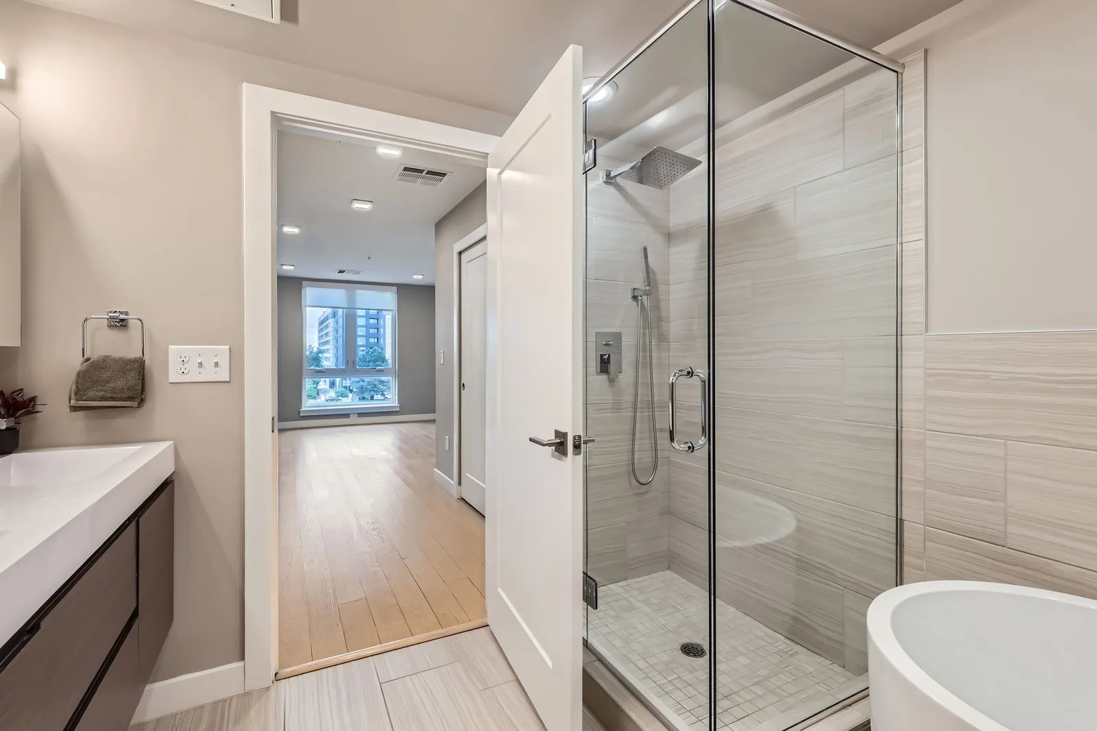 Modern bathroom with a glass walk-in shower and separate bathtub in a luxury apartment at The Julian, Sloans Lake, Denver, looking into another room.