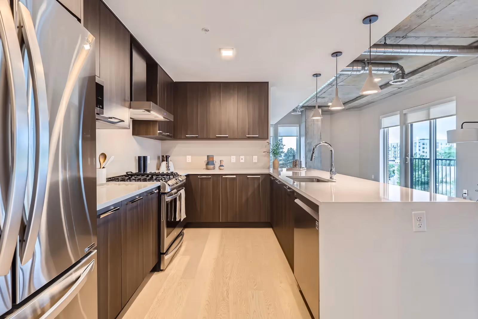 Sleek kitchen with dark wood cabinets, stainless steel appliances, and a large white island with a sink in an apartment at The Julian, Sloans Lake, Denver.