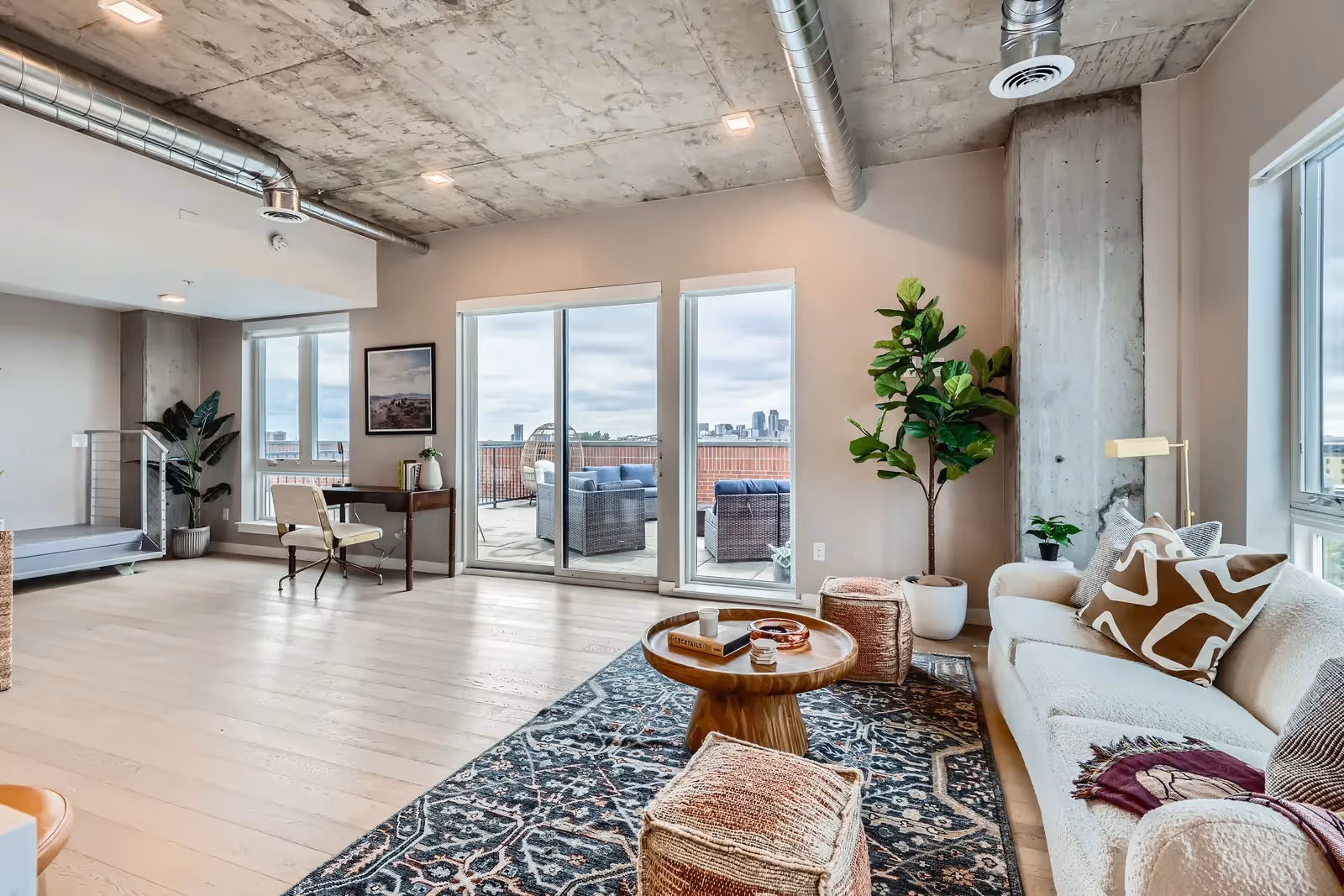 Luxurious living room in a penthouse apartment at The Julian, Sloans Lake, Denver, featuring a work desk, comfortable seating, and sliding glass doors to a balcony with city views.