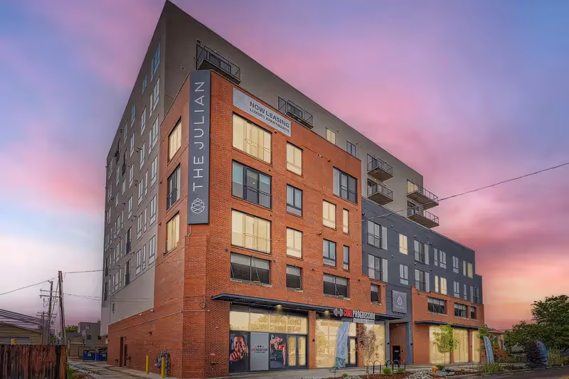 Exterior view of The Julian luxury apartment building in Sloans Lake, Denver, Colorado, at dusk, showcasing its modern architecture and "Now Leasing" sign.