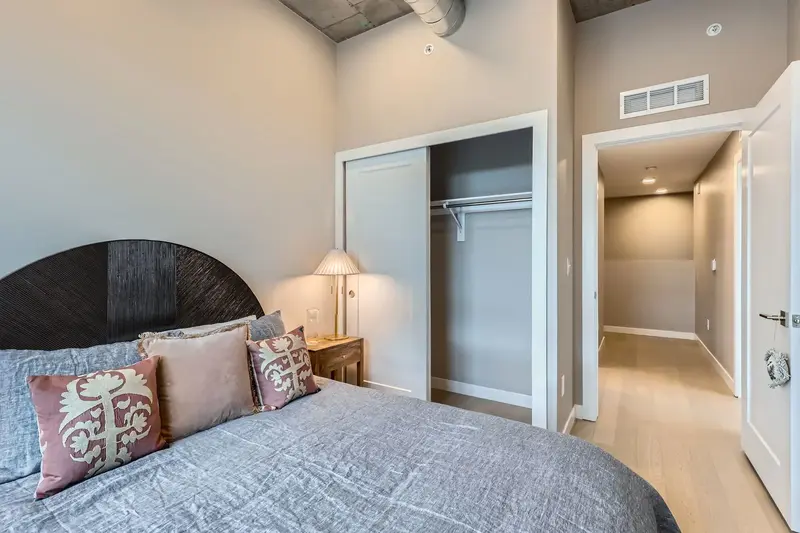 Bedroom in a luxury apartment at The Julian in Sloans Lake, Denver, with a stylish bed, exposed concrete ceiling, and a sliding closet door.