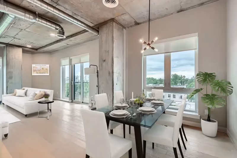 Modern dining area in a luxury apartment at The Julian in Sloans Lake, Denver, with a glass table, white chairs, and large windows overlooking the city.