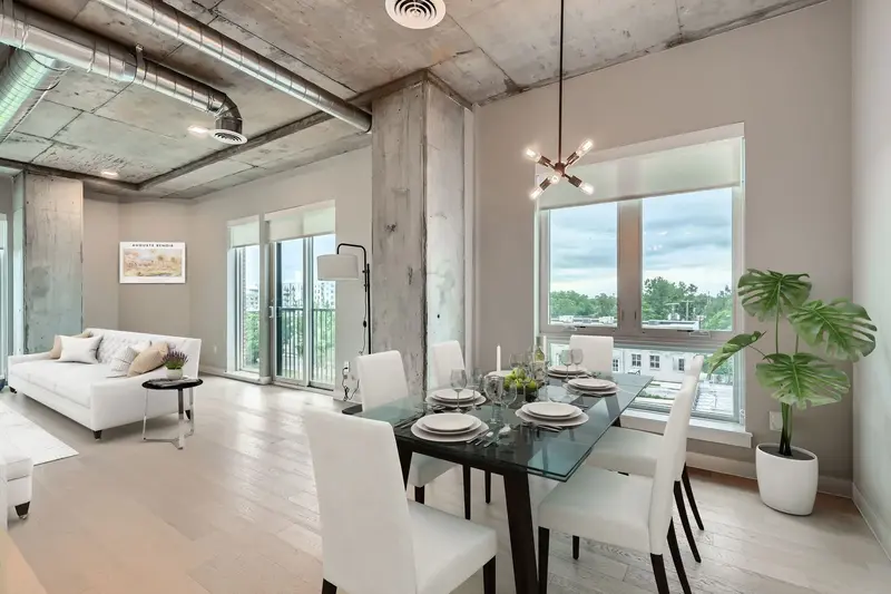 Modern dining area in a luxury apartment at The Julian in Sloans Lake, Denver, with a glass table, white chairs, and large windows overlooking the city.
