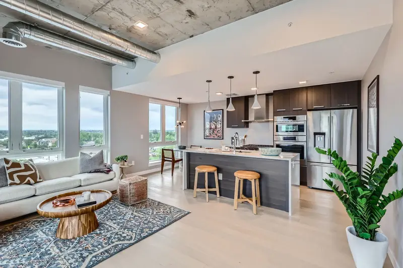 Open-concept living room and kitchen in a luxury apartment at The Julian in Sloans Lake, Denver, with concrete ceilings, modern appliances, and city views.