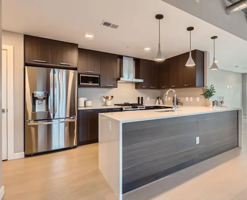 Gourmet kitchen in a luxury apartment at The Julian in Sloans Lake, Denver, featuring dark wood cabinetry, stainless steel appliances, and a large island.