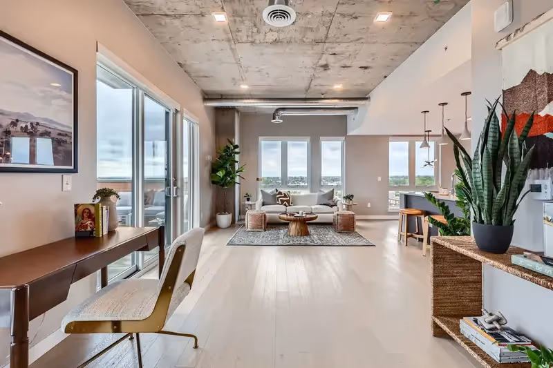 Expansive open-concept living space in a luxury apartment at The Julian in Sloans Lake, Denver, with concrete ceilings, large windows offering city views, and modern furnishings.