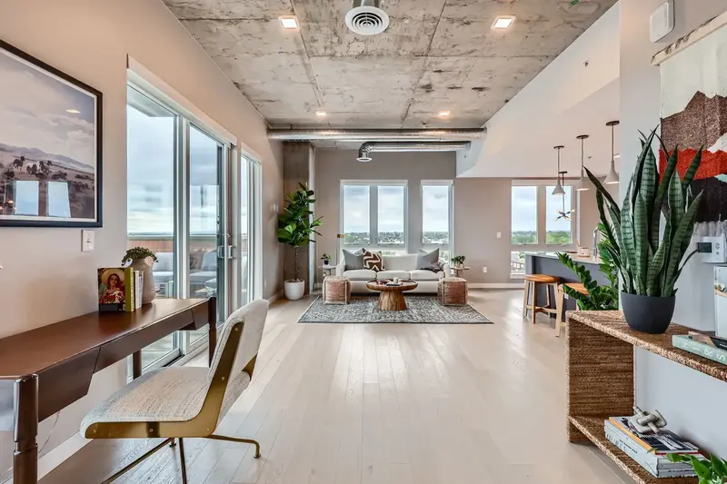Expansive open-concept living space in a luxury apartment at The Julian in Sloans Lake, Denver, with concrete ceilings, large windows offering city views, and modern furnishings.