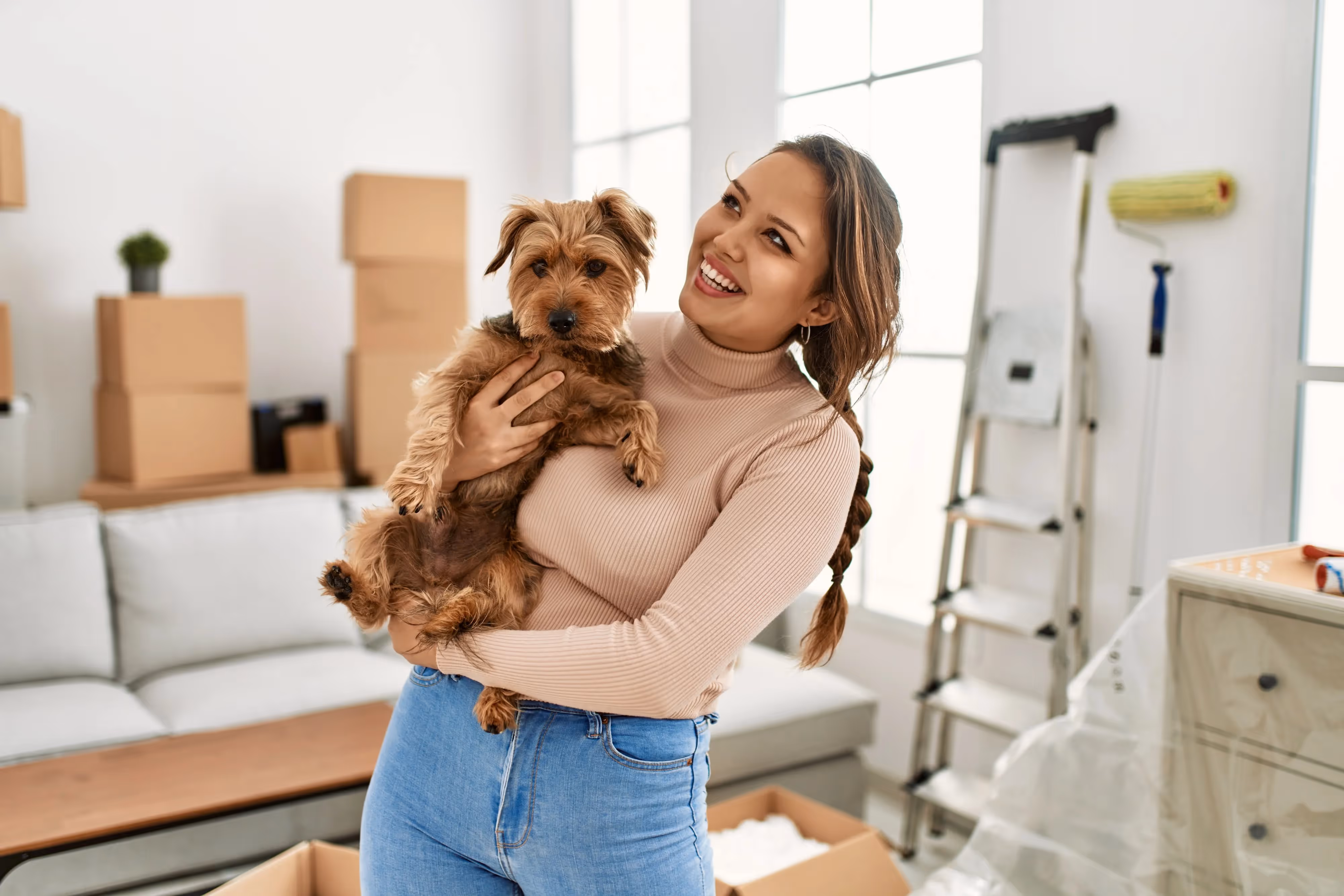 Happy woman holding a small dog in a new apartment filled with moving boxes, representing pet-friendly living at The Julian in Sloans Lake, Denver, CO.
