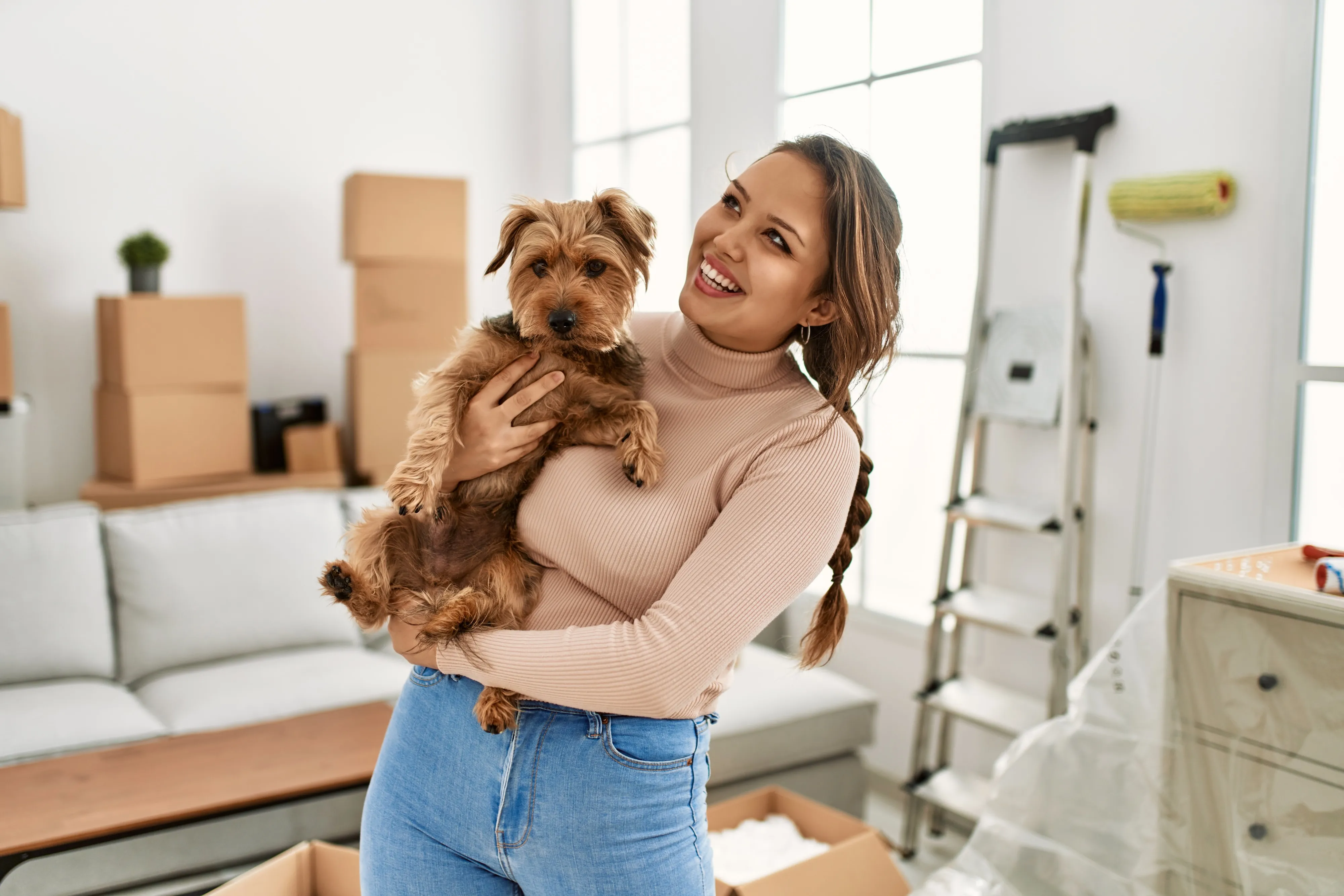 Happy woman holding a small dog in a new apartment filled with moving boxes, representing pet-friendly living at The Julian in Sloans Lake, Denver, CO.