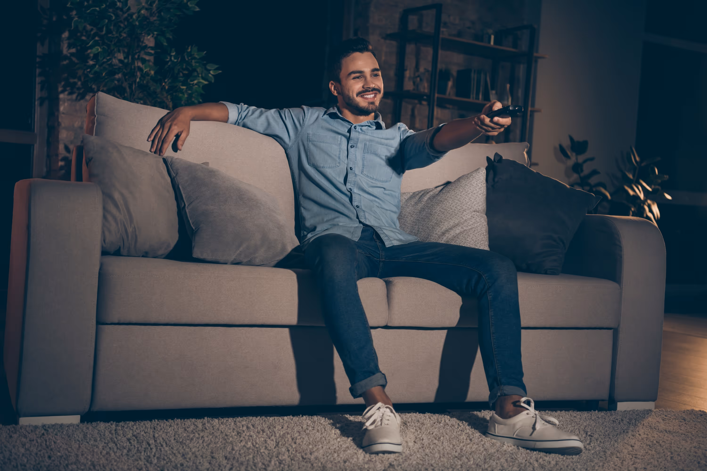 A happy man relaxing on a comfortable sofa and watching TV in a modern media room, depicting a serene living environment at The Julian in Denver, CO.
