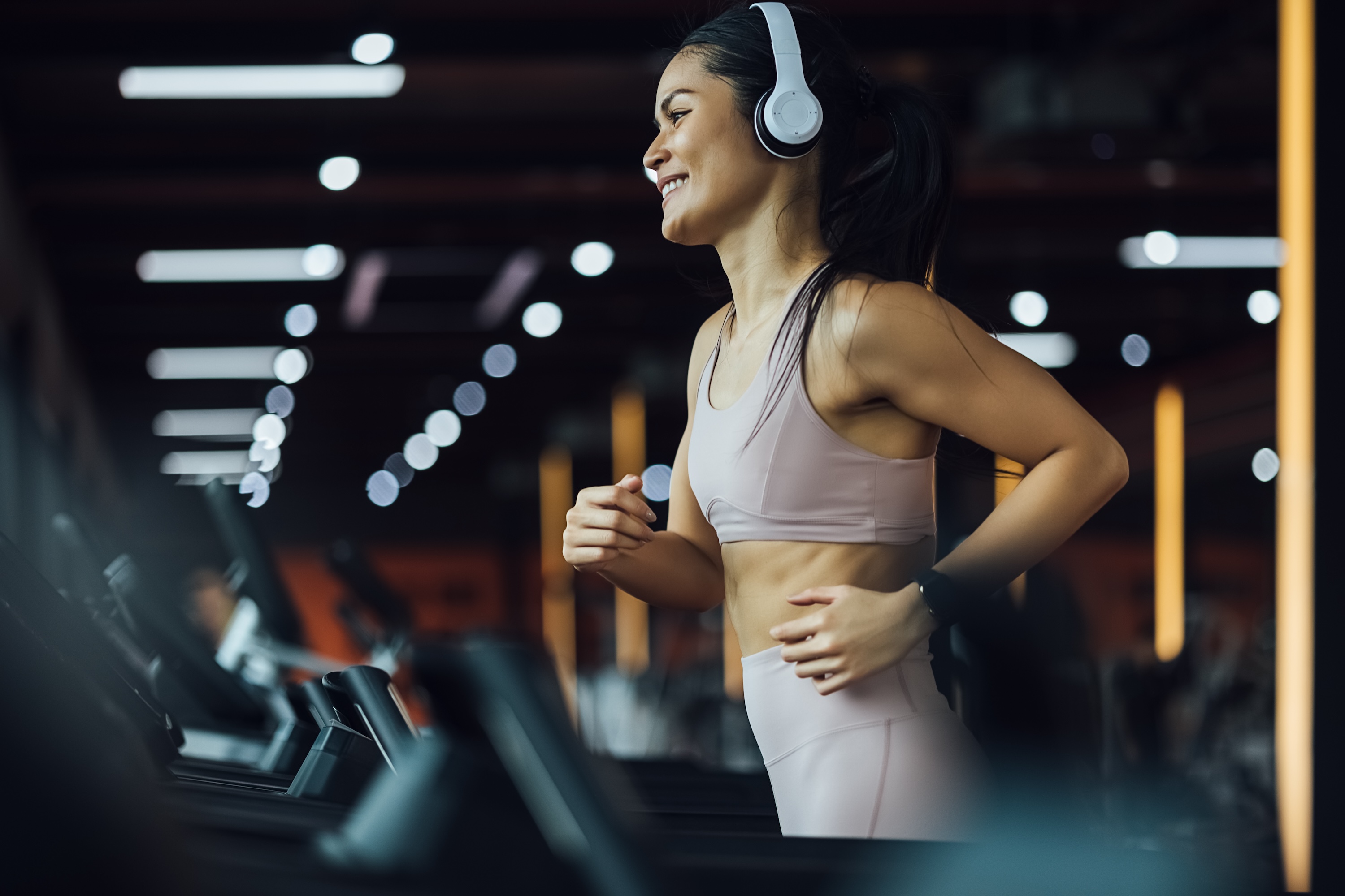 A smiling woman wearing headphones and running on a treadmill, representing the state-of-the-art fitness amenities at The Julian in Sloans Lake, CO.