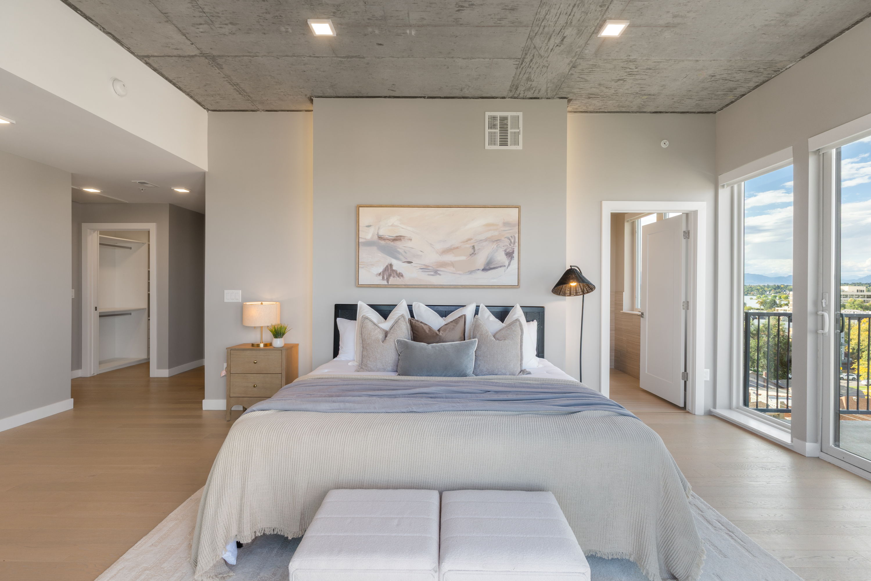 Bedroom in a luxury apartment at The Julian in Sloans Lake, Denver, with a stylish bed, exposed concrete ceiling, and a sliding closet door.