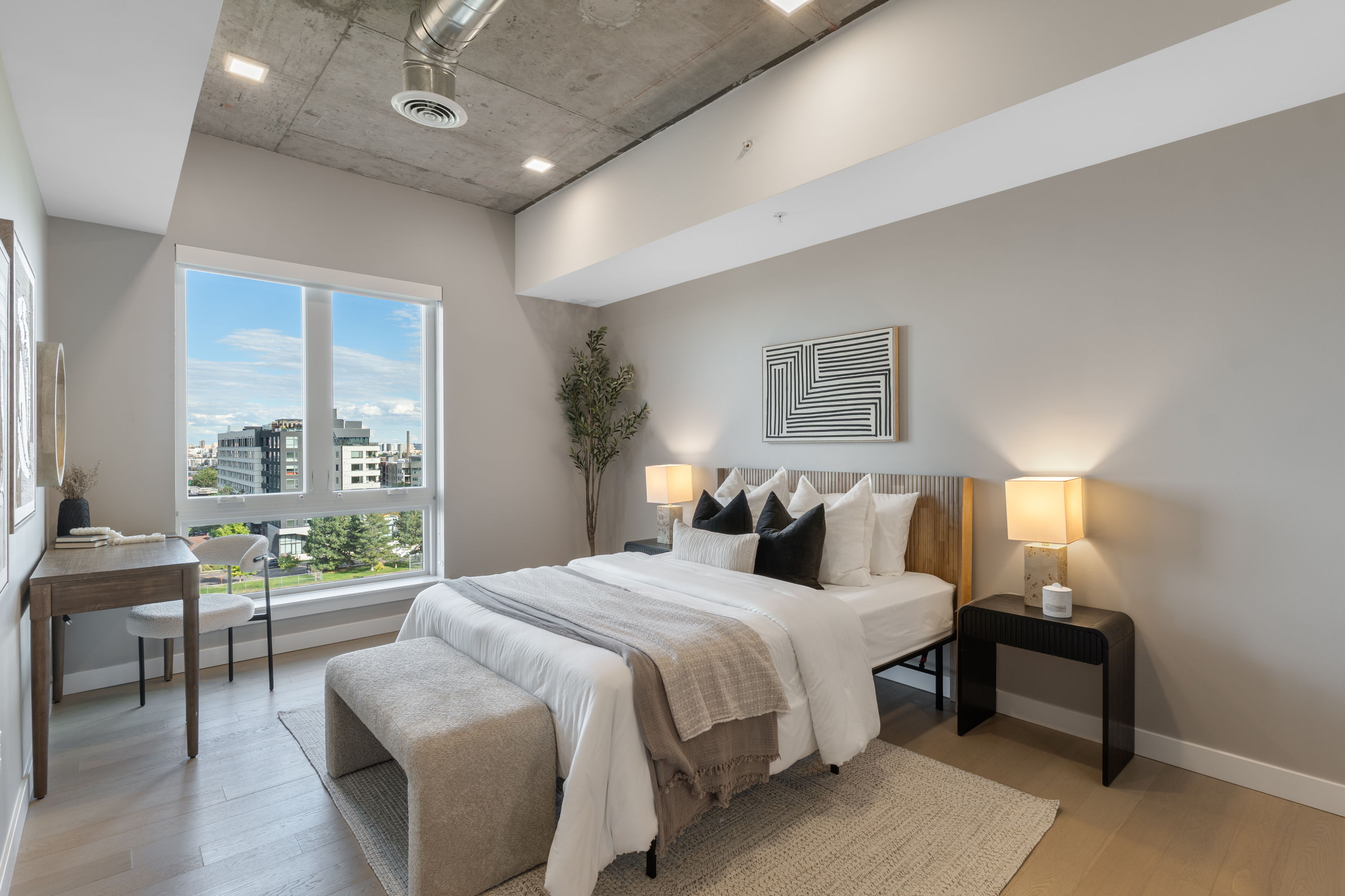 Modern bedroom with large window overlooking Sloans Lake and Denver cityscape, featuring a stylish bed and full-length mirror, at The Julian apartments.