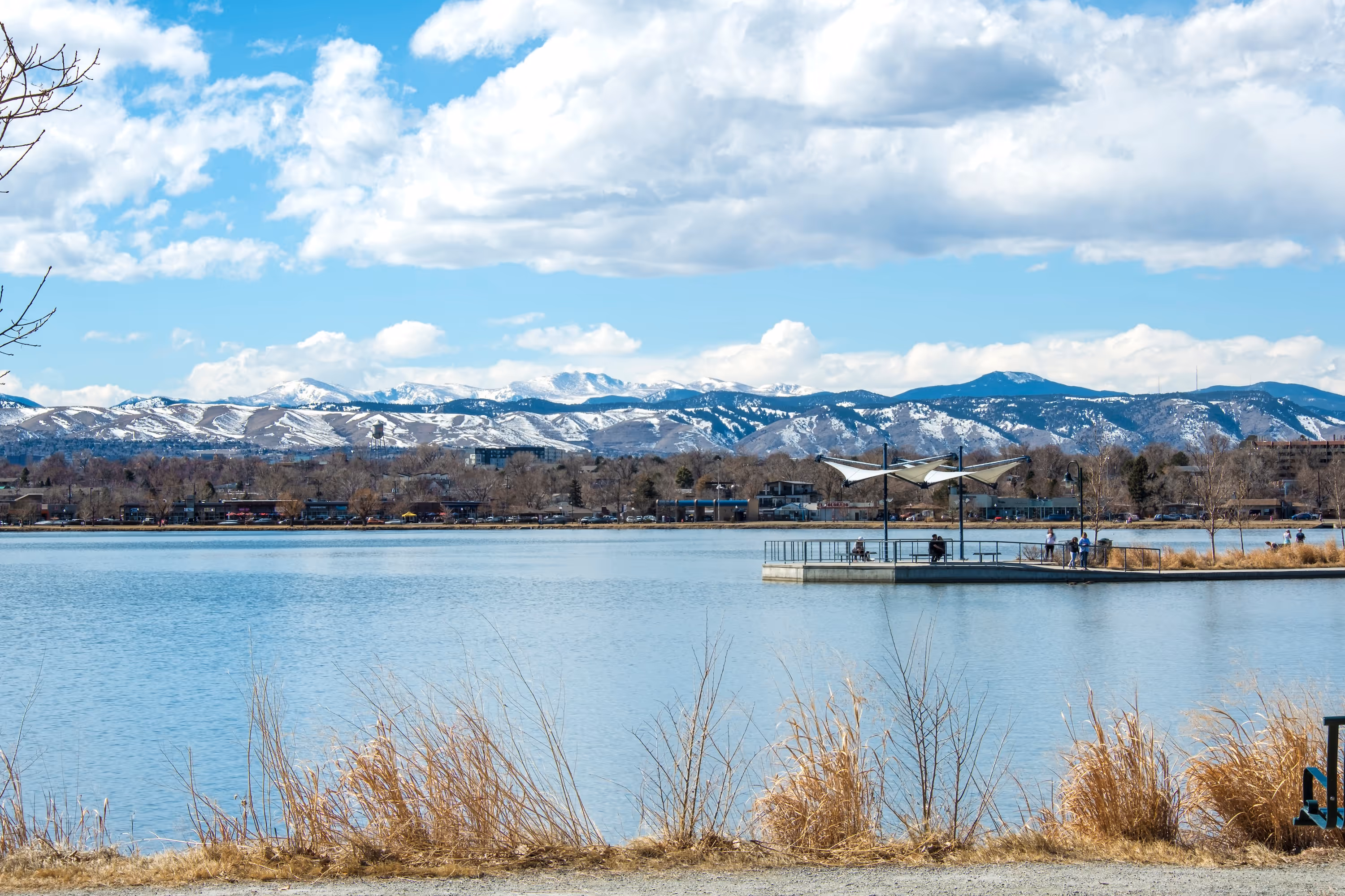 Scenic view of a lake with a walking pier and snow-capped mountains in the background in Denver.
