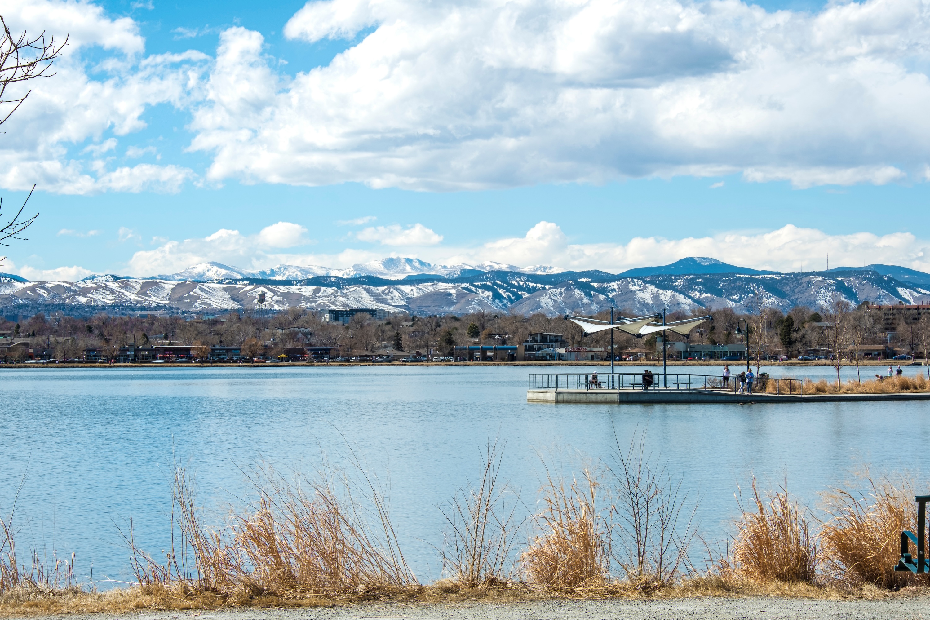 Scenic view of a lake with a walking pier and snow-capped mountains in the background in Denver.