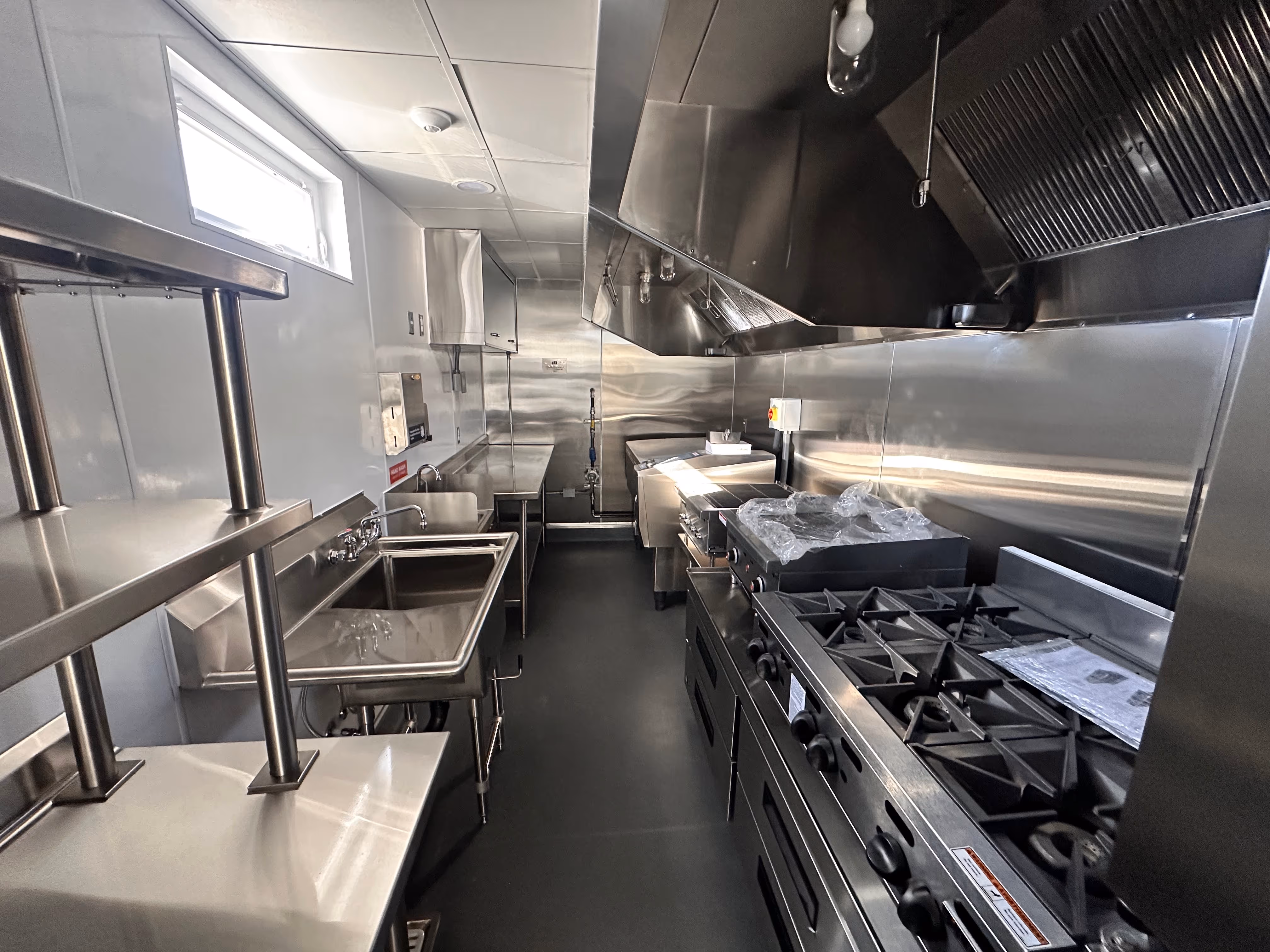 Interior of a clean, modern commercial kitchen with stainless steel appliances, sinks, and cooking equipment.