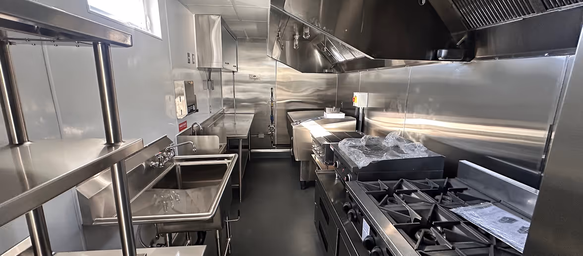Modern commercial kitchen with stainless steel appliances, multiple sinks, and cooking equipment.