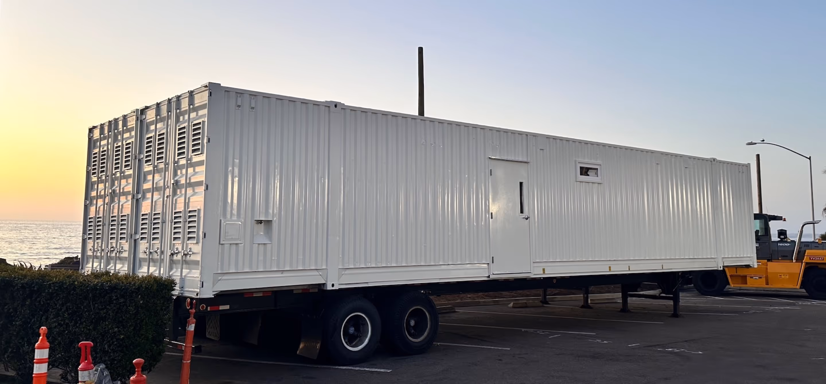 White shipping container trailer parked in a lot by the ocean at sunset.
