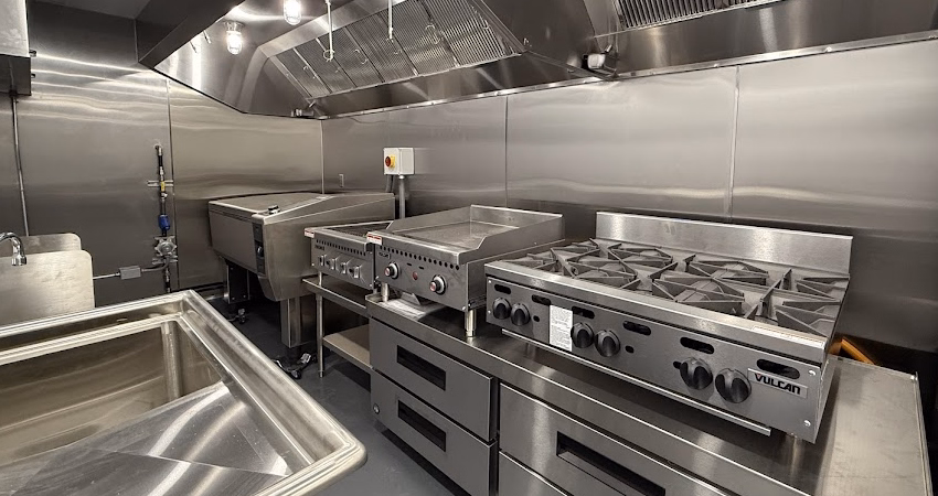 Modern commercial kitchen with stainless steel appliances including a multi-burner stove, griddle, and ovens.