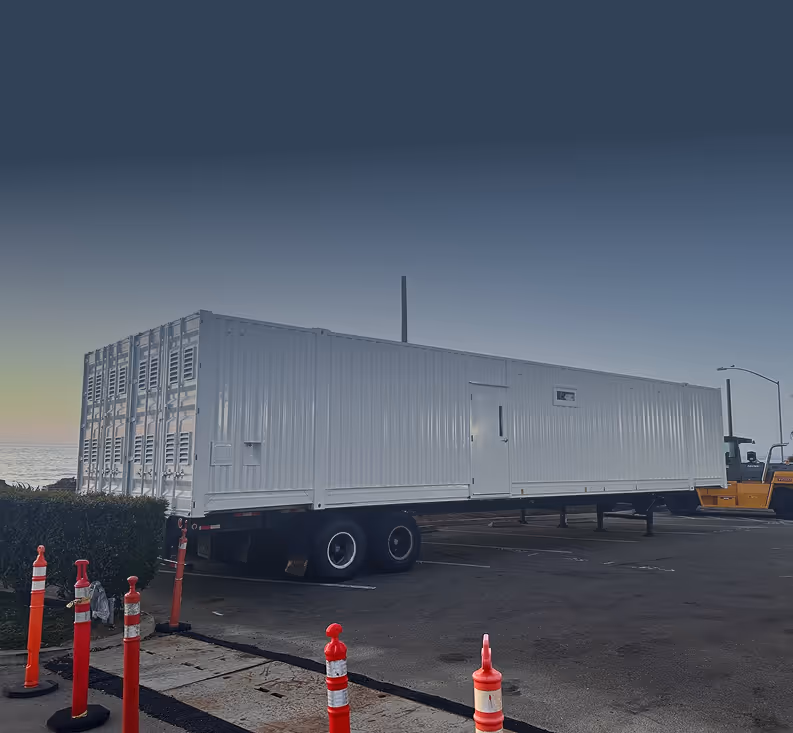 White mobile kitchen trailer parked in a lot near orange traffic cones at dusk.