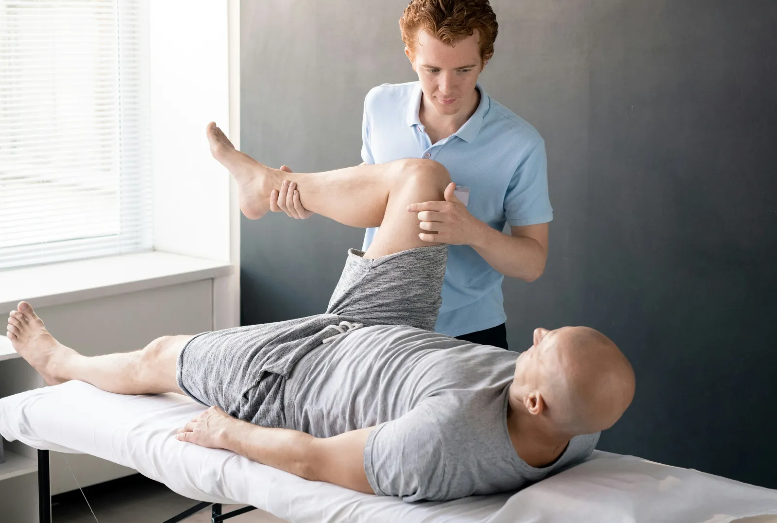 Fizjoterapeuta wykonuje cwiczenie ze swoim pacjentem który leży na plecach.