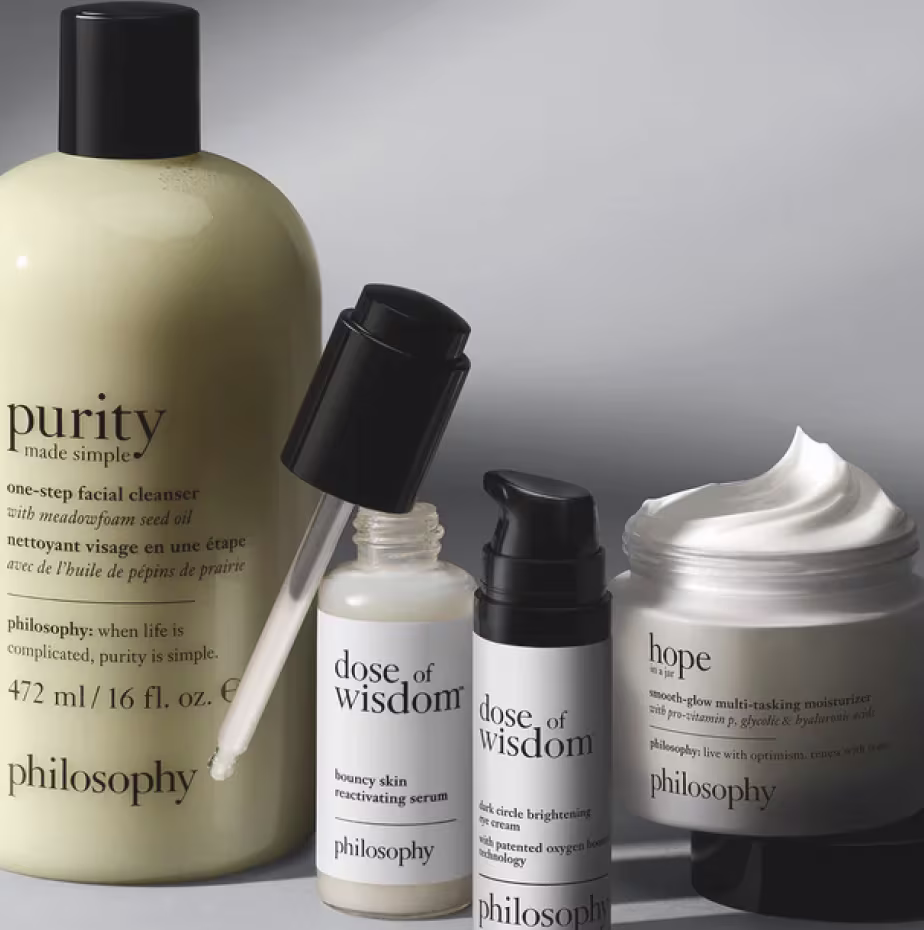 Philosophy skincare products, including Purity cleanser, Dose of Wisdom serums, and Hope moisturizer, displayed against a soft gray background.