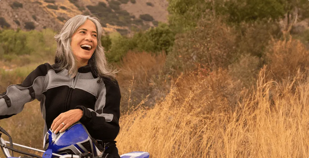 A lady on top of a motorcycle, she's smiling at the a spot far from the camera