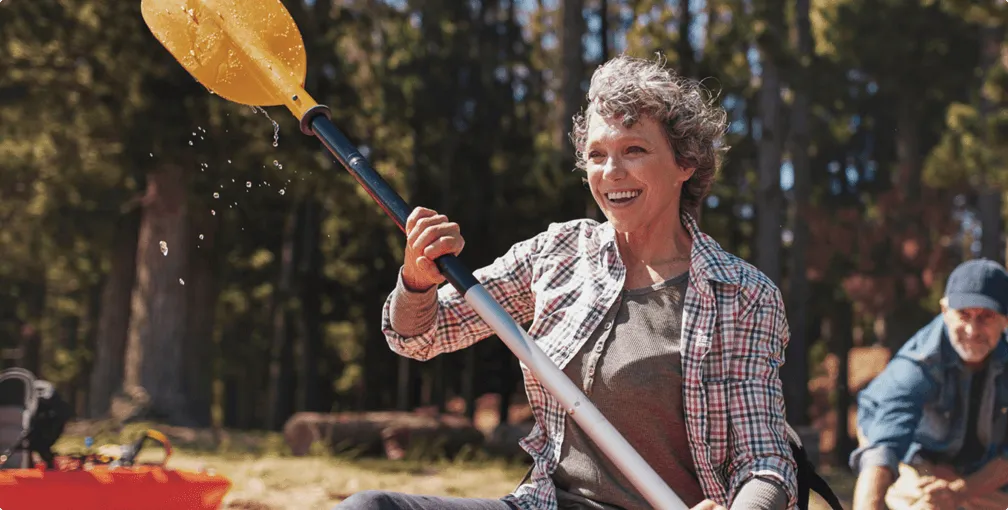 A lady paddling, there's a forest behind her, she looks very happy