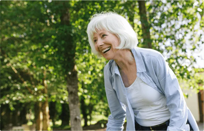 A lady smiles happily, there are trees around her