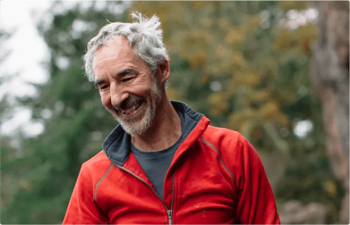 A man smiles, there are trees behind him in the distance