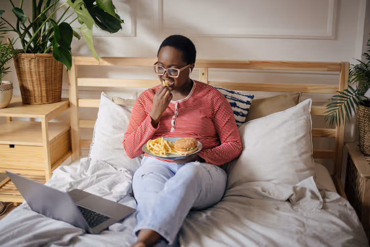 Woman eating sandwich and french fries on bed