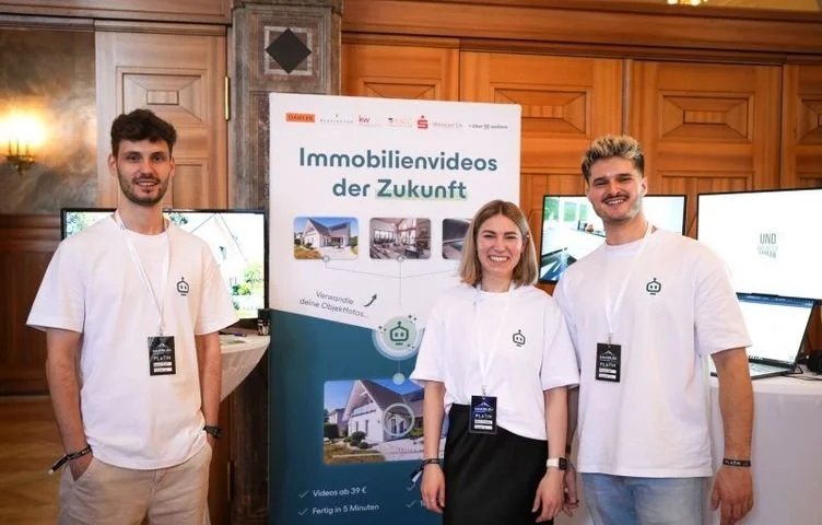 Drei Leute aus dem marton.ai-Team in weißen marton-Shirts vor einem Roll-up mit der Aufschrift „Immobilienvideos der Zukunft“