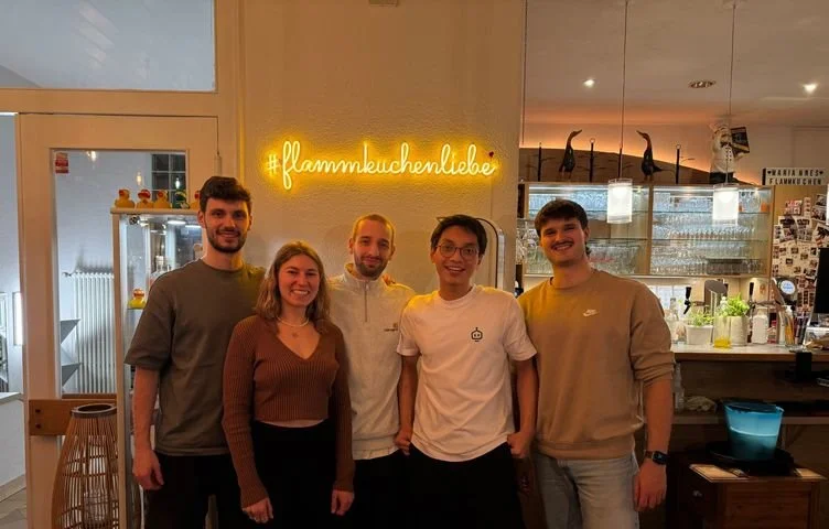 Fünf Leute aus dem Team in einem Restaurant vor dem Leuchtschriftzug „#flammkuchenliebe“