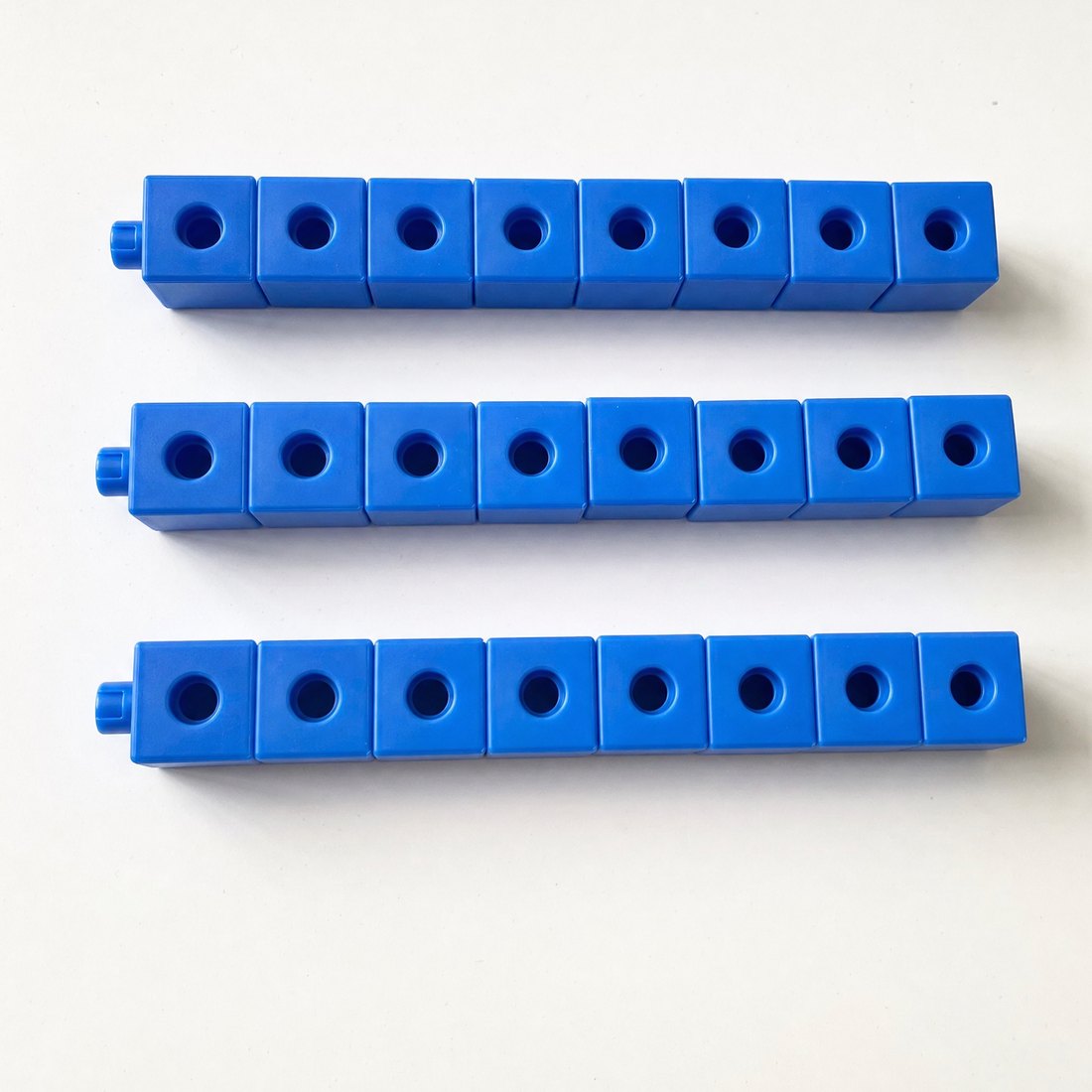 Photograph of 24 blue connecting cubes snapped into three rows of eight, lying on a white desk.