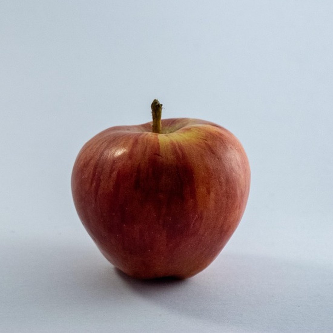 Photograph of a single red apple on a white surface.