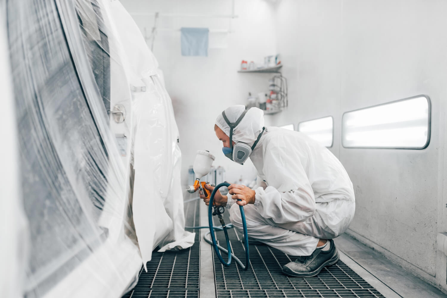 Technician in white suit spray-painting car in San Antonio auto body shop.