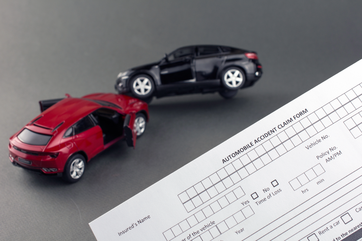 Red and black toy cars crash with accident claim form.
