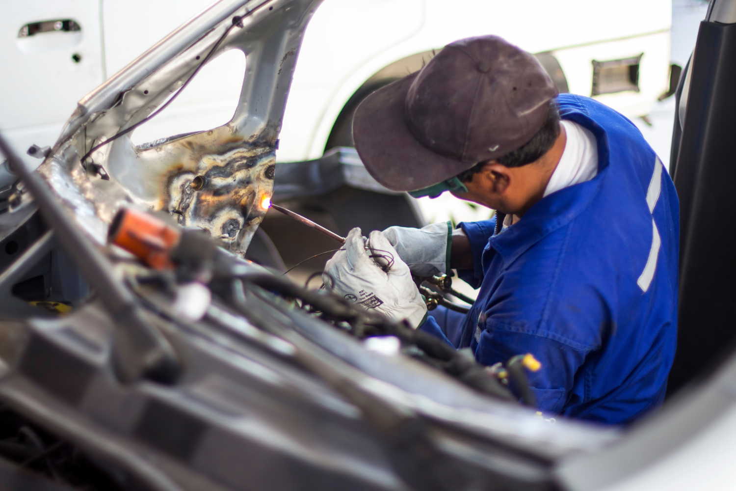Mechanic welding car frame in auto body shop.
